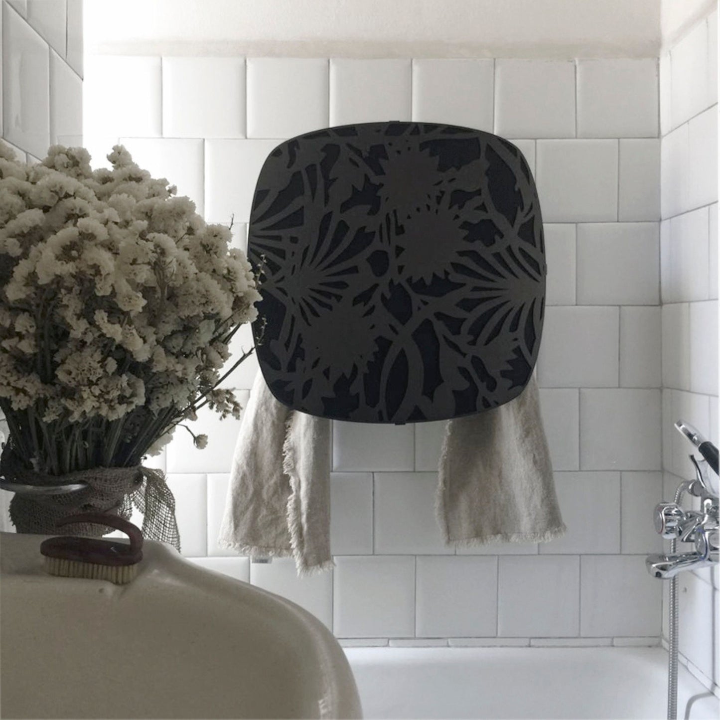 schwarze Abdeckung aus Metall, Blumenmuster, mit Lücken, durch die der schwarze Handtuchwärmer dahinter zu sehen ist
