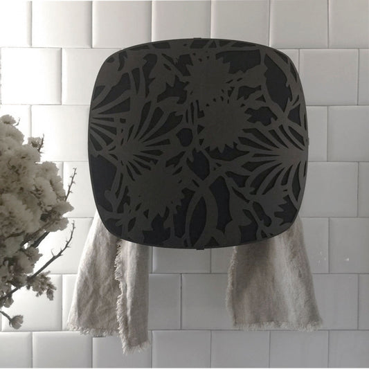 schwarze Abdeckung aus Metall, Blumenmuster, mit Lücken, durch die der Handtuchwärmer dahinter zu sehen ist